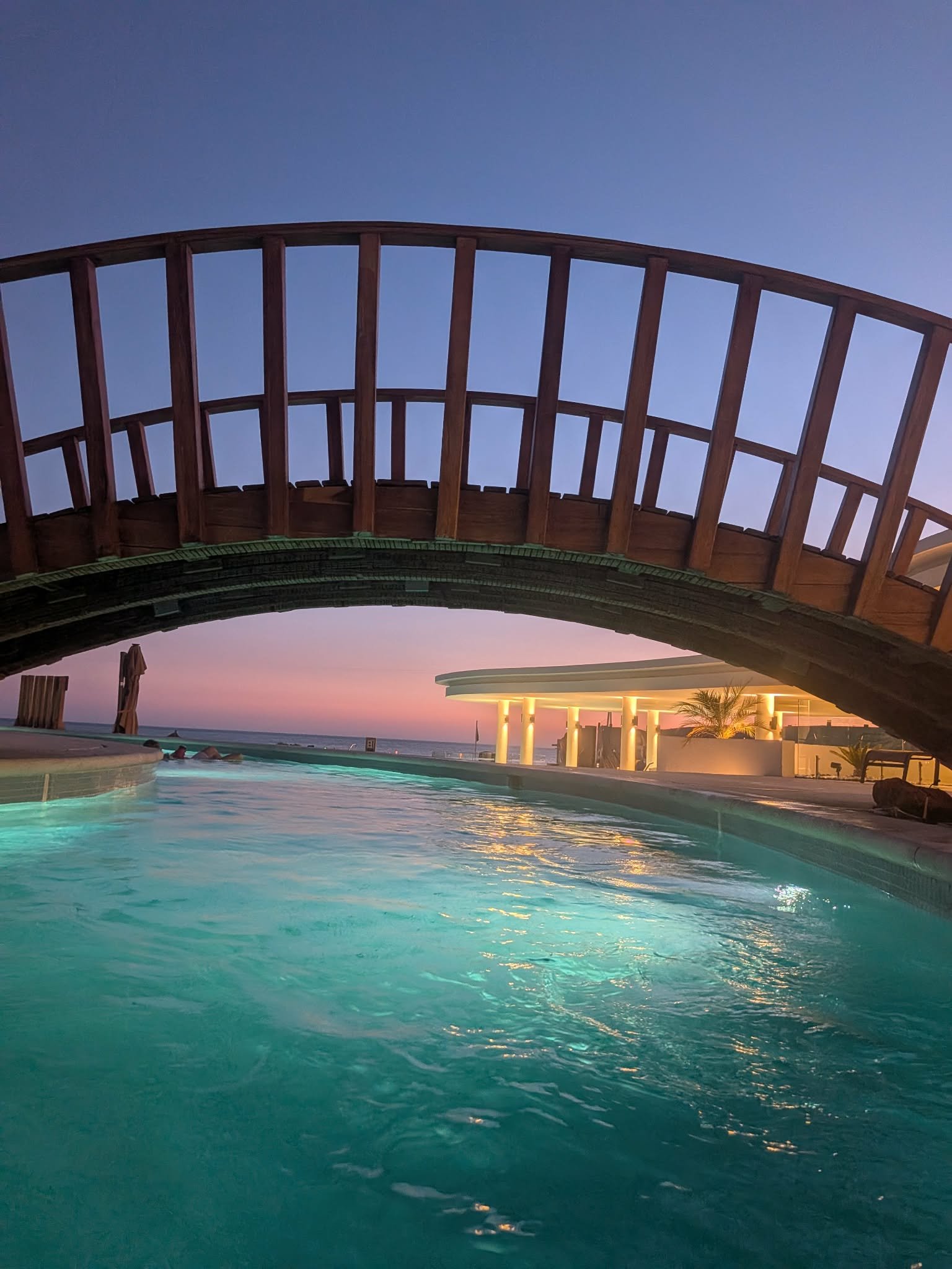 Resort lazy river glowing turquoise beneath a wooden bridge at sunset